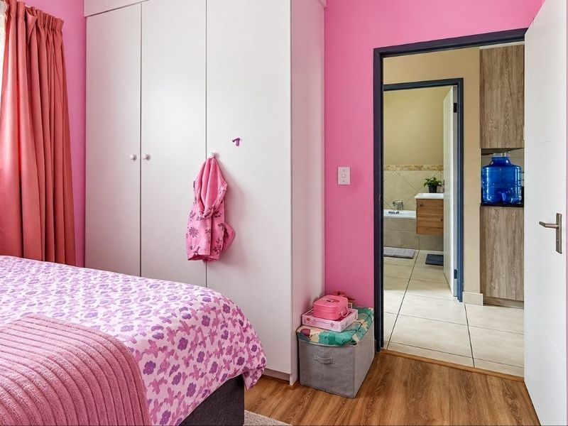 A bedroom featuring built-in cupboards and laminate flooring, with a view through the doorway into an adjacent bathroom area.