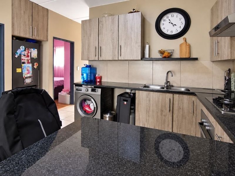 A functional kitchen featuring granite countertops, wood-finish cabinetry, a gas hob with extractor fan, and integrated space for laundry appliances.