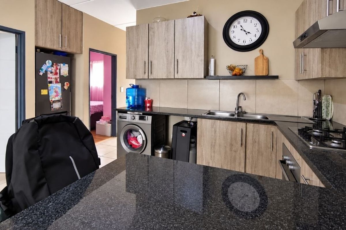 A functional kitchen featuring granite countertops, wood-finish cabinetry, a gas hob with extractor fan, and integrated space for laundry appliances.