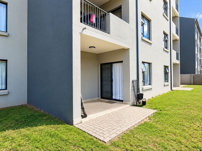 Rear view of the apartment building featuring a paved ground-floor patio, sliding door access, and a small private lawn area.