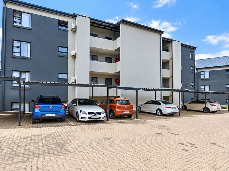 Exterior view of a modern apartment complex featuring a paved parking area with covered bays and multi-story residential units.