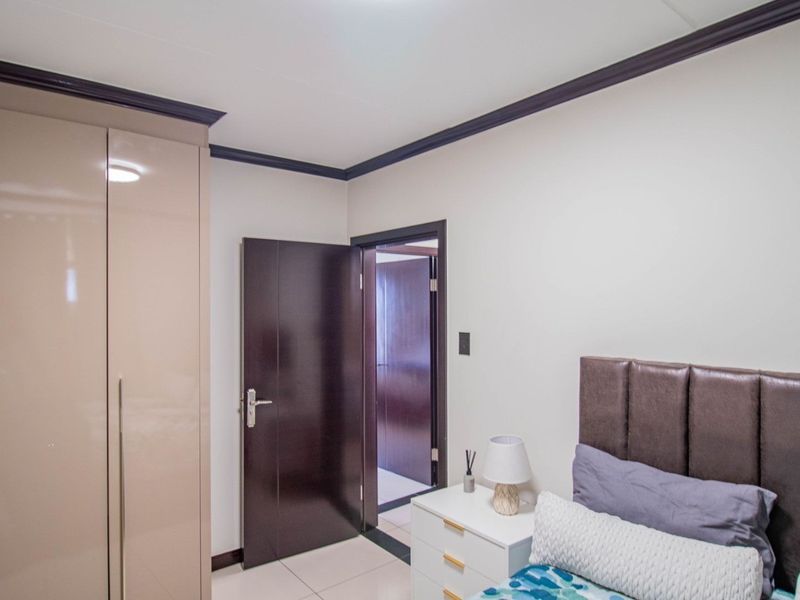 A well-maintained bedroom featuring high-gloss built-in wardrobes, dark wood doors, and neutral tiled flooring with decorative crown molding.