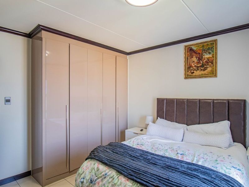 A well-maintained bedroom featuring high-gloss built-in wardrobes, crown molding, and tiled flooring, with an adjacent view into a tiled bathroom.