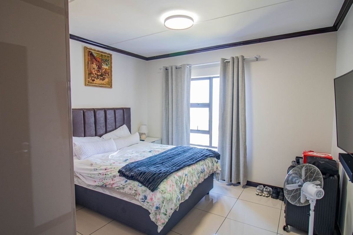 A well-lit bedroom featuring tiled flooring, crown molding, and a window, providing a functional and comfortable living space.
