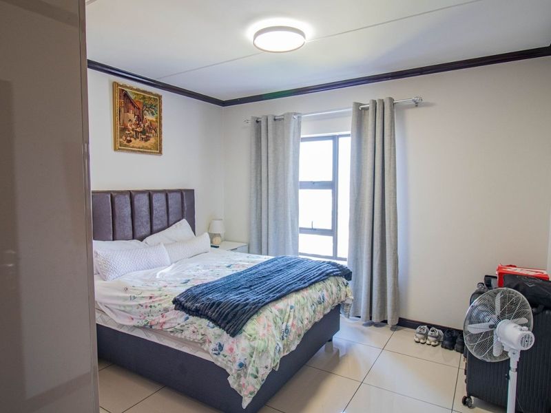 A well-lit bedroom featuring tiled flooring, crown molding, and a window, providing a functional and comfortable living space.