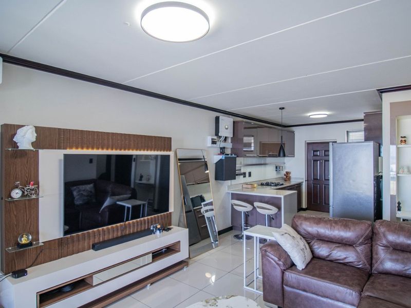 An open-plan living and kitchen area featuring a modern built-in media unit, sleek kitchen cabinetry with a breakfast bar, and tiled flooring throughout.