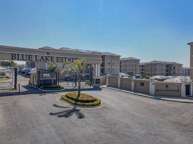 Aerial view of the main entrance and security gate of Blue Lake Estate, featuring paved driveways and multi-story apartment buildings.