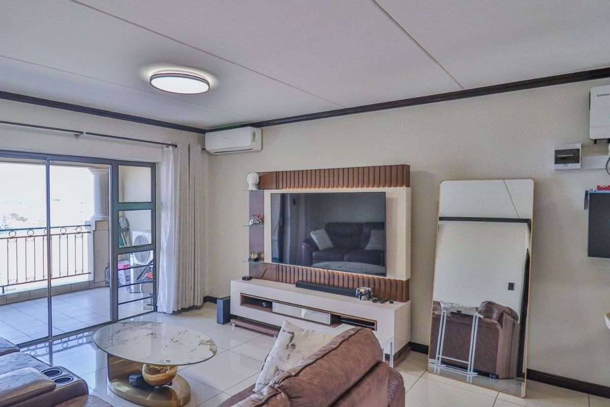 A well-maintained living room featuring tiled floors, a built-in media wall, air conditioning, and direct access to a private balcony.