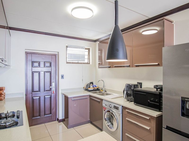 Modern kitchen featuring high-gloss cabinetry, gas hob, extractor fan, and integrated laundry plumbing, finished with neutral tiled flooring and contemporary lighting.