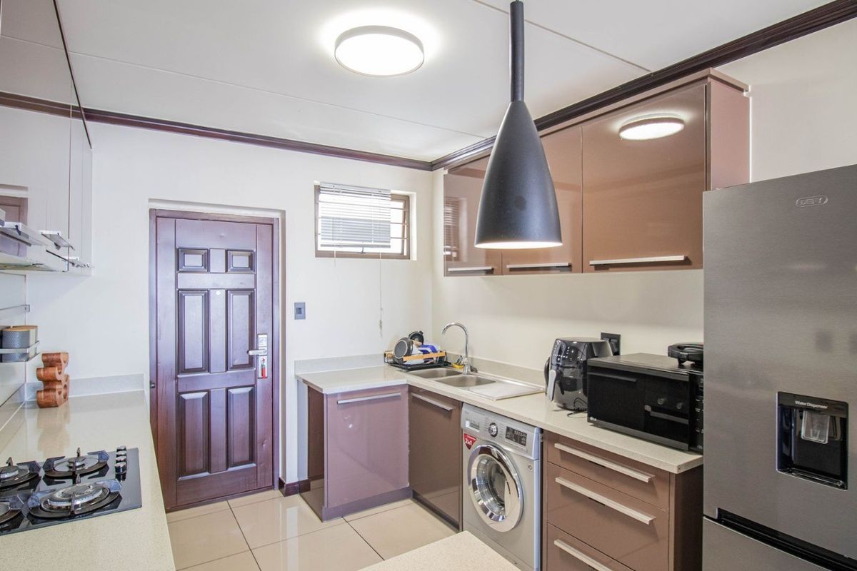 Modern kitchen featuring high-gloss cabinetry, gas hob, extractor fan, and integrated laundry plumbing, finished with neutral tiled flooring and contemporary lighting.