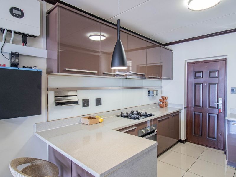 Modern kitchen featuring high-gloss cabinetry, stone countertops, integrated gas hob and oven, and a wall-mounted solar inverter system.