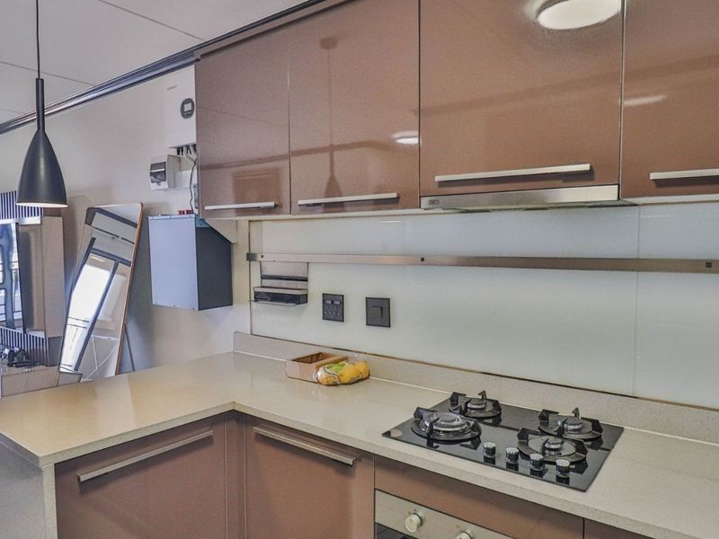 Modern kitchen featuring high-gloss cabinetry, stone countertops, a gas hob, built-in oven, and integrated extractor fan, seamlessly flowing into the adjacent living area.