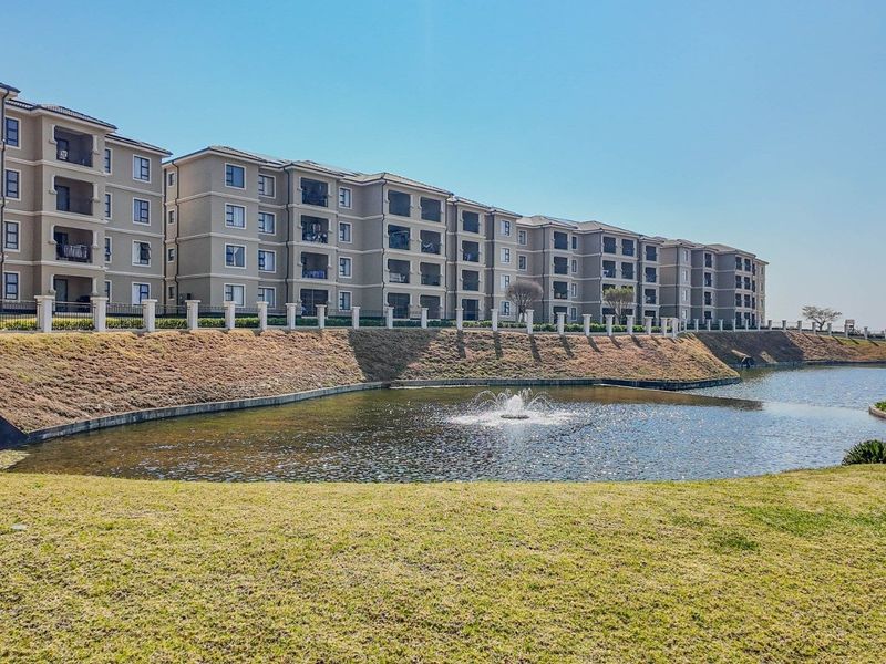 Exterior view of a multi-story apartment complex featuring private balconies, landscaped grounds, and a central water feature.