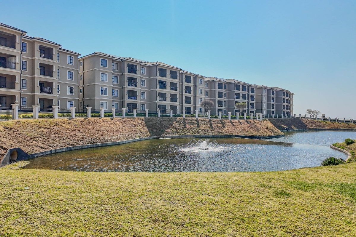 Exterior view of a multi-story apartment complex featuring private balconies, landscaped grounds, and a central water feature.