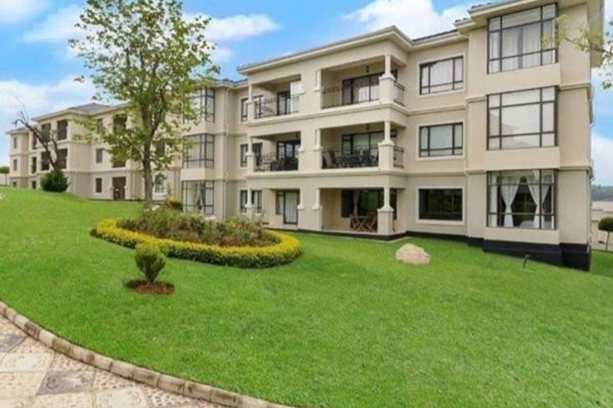 A view of the rear elevation of a multi-story apartment complex featuring private balconies, large windows, and well-maintained landscaped garden areas.