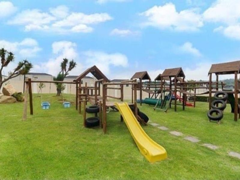 A well-maintained communal garden area featuring a wooden playground structure with slides and swings set on a grassy lawn.