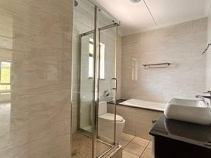 Modern bathroom featuring a glass shower enclosure, built-in bathtub, wall-mounted toilet, and a vessel sink set on a vanity cabinet with tiled finishes.