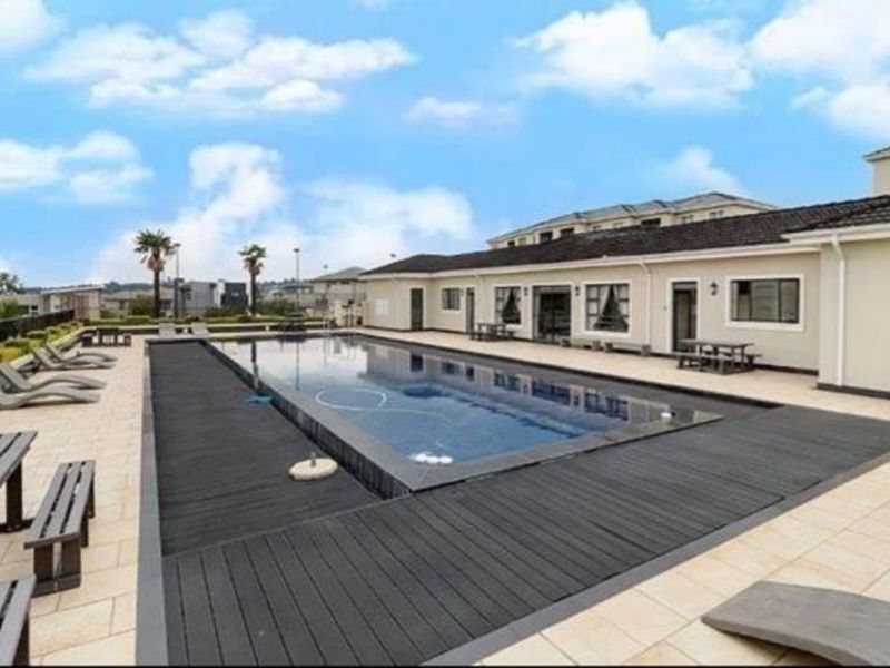 A well-maintained communal swimming pool area featuring a tiled deck, composite wood surround, and direct access to the apartment building exterior.