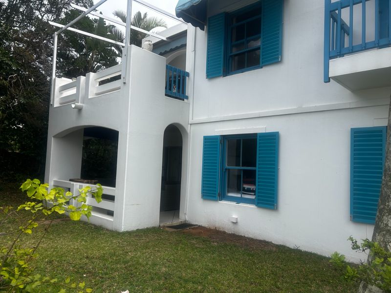 Rear view of the apartment building featuring a ground-floor patio, upper-level balcony, and blue window shutters.