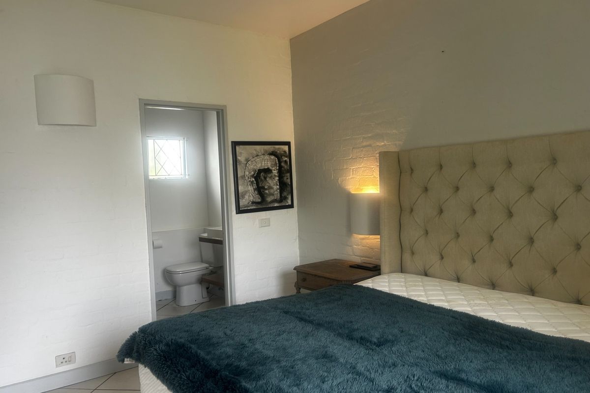 A bedroom featuring an exposed brick wall, tiled flooring, and direct access to an en-suite bathroom with a toilet.