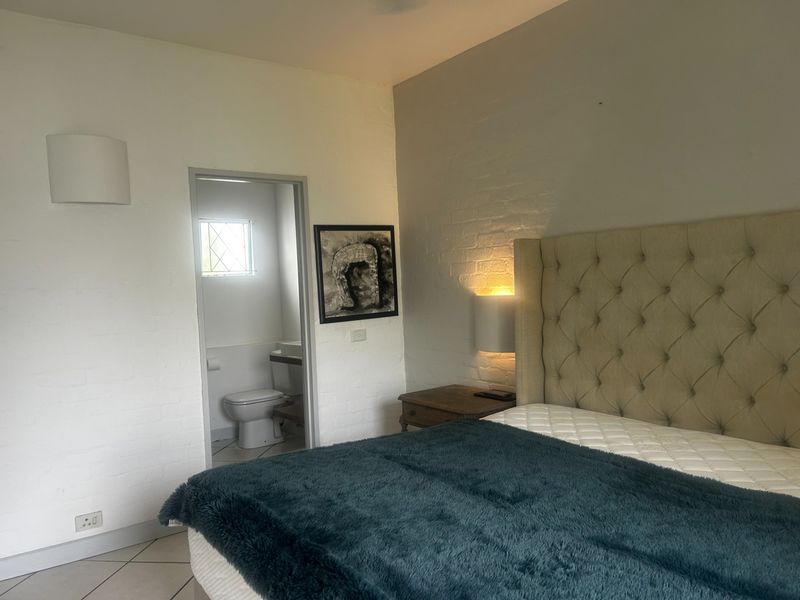 A bedroom featuring an exposed brick wall, tiled flooring, and direct access to an en-suite bathroom with a toilet.