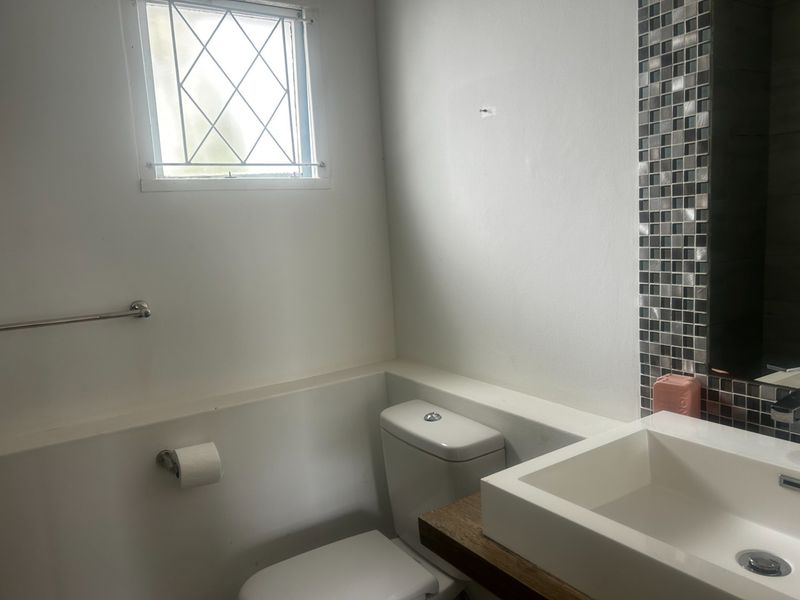 A compact bathroom featuring a modern vessel sink on a wooden vanity, mosaic tile accents, and a toilet with a window.