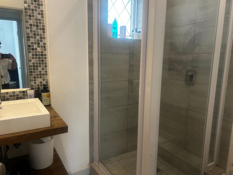 A modern bathroom featuring a vessel sink on a wooden vanity, mosaic tile accents, and a glass-enclosed shower with neutral wall tiling.