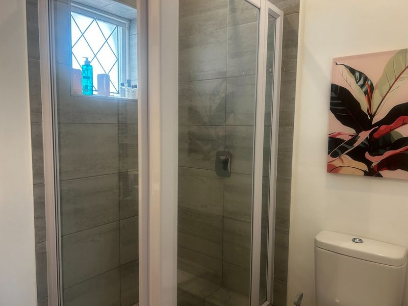 A functional bathroom featuring a glass-enclosed shower with modern grey wall tiles and a standard toilet.