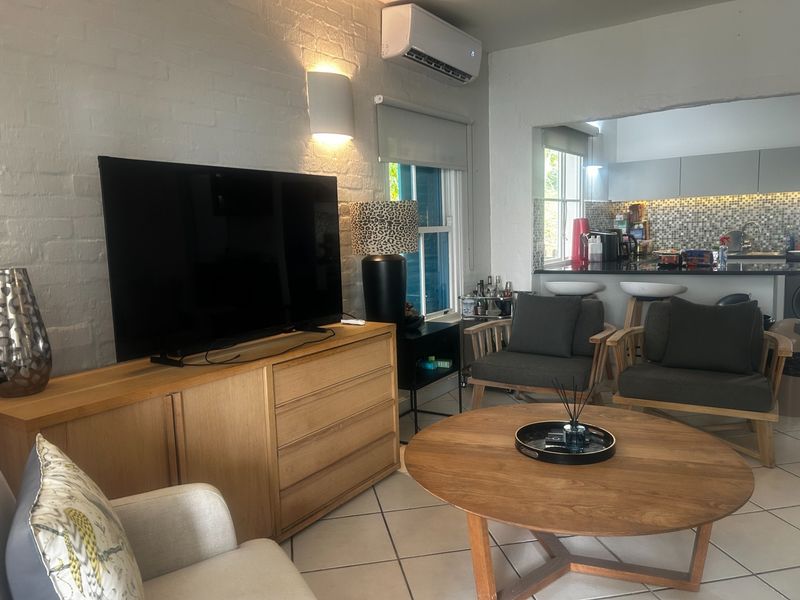 Open plan living area featuring tiled floors, exposed brick walls, split-system air conditioning, and a breakfast bar connecting to the kitchen.