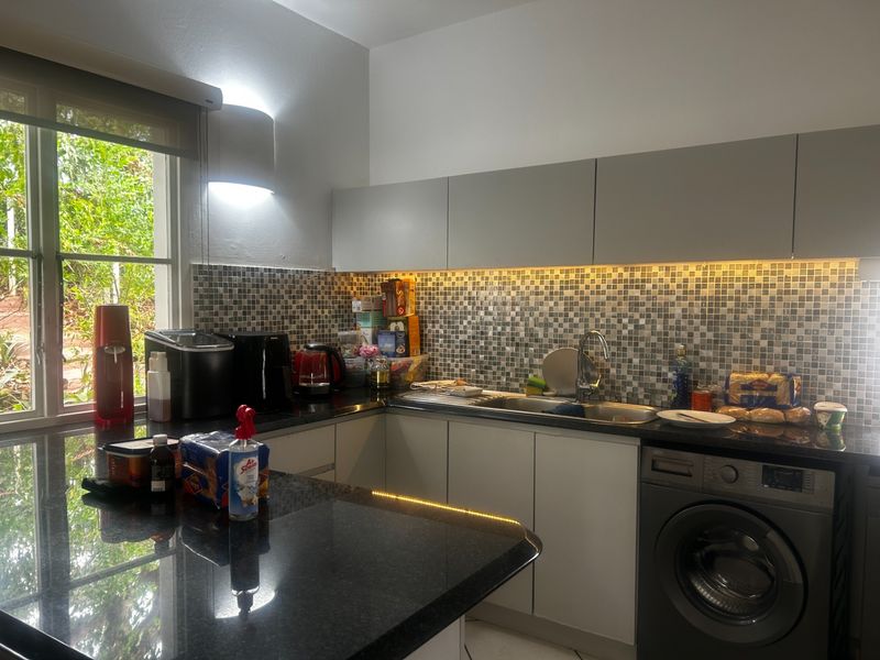 Modern kitchen featuring granite countertops, mosaic tile backsplash, under-cabinet LED lighting, and an integrated washing machine with handleless cabinetry.