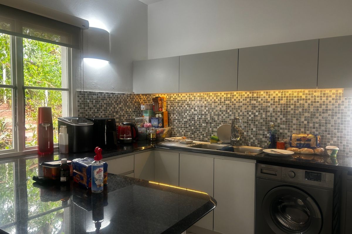 Modern kitchen featuring granite countertops, mosaic tile backsplash, under-cabinet LED lighting, and an integrated washing machine with handleless cabinetry.