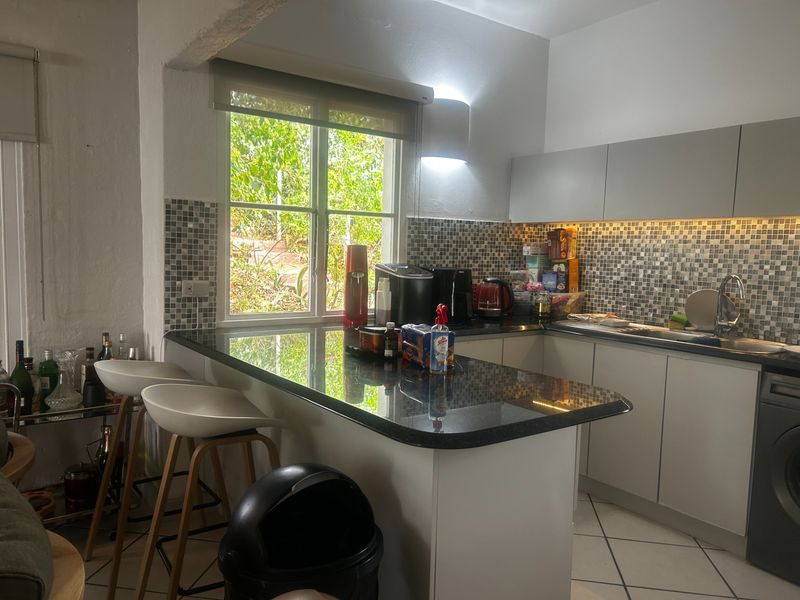 Modern kitchen featuring granite countertops, a breakfast bar, mosaic tile backsplash, and integrated under-cabinet lighting with a view of the garden.