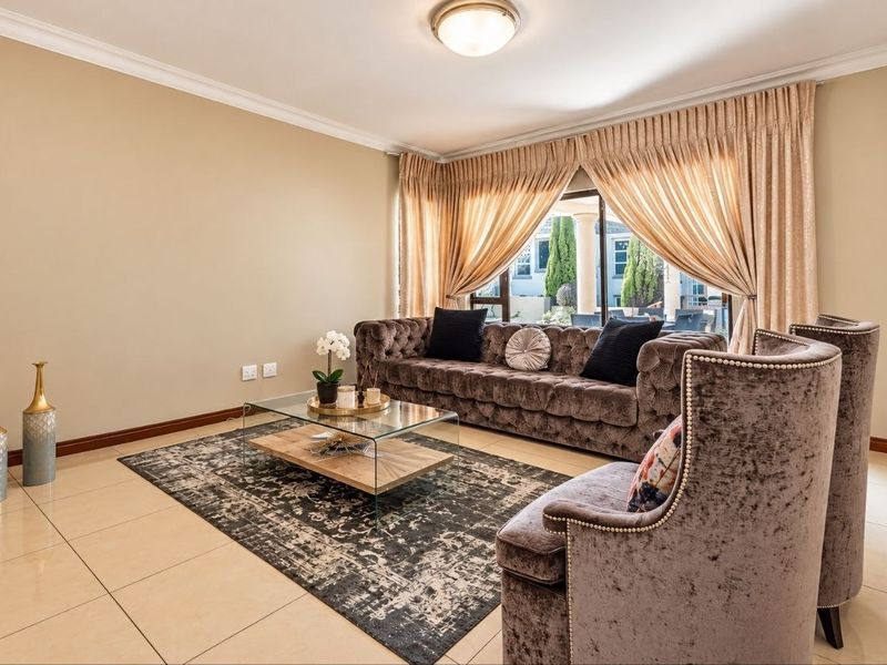 A well-maintained living room featuring neutral tiled flooring, coved cornicing, and a large sliding glass door providing natural light and access to the patio.