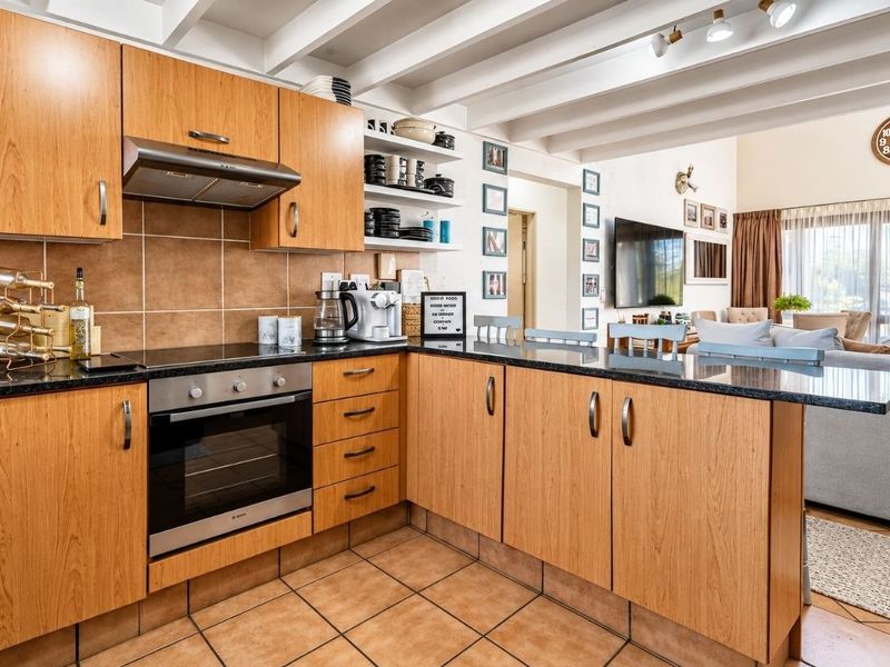 Open-plan kitchen featuring wooden cabinetry, granite countertops, built-in oven, and extractor fan, seamlessly flowing into the adjacent living area with exposed ceiling beams.