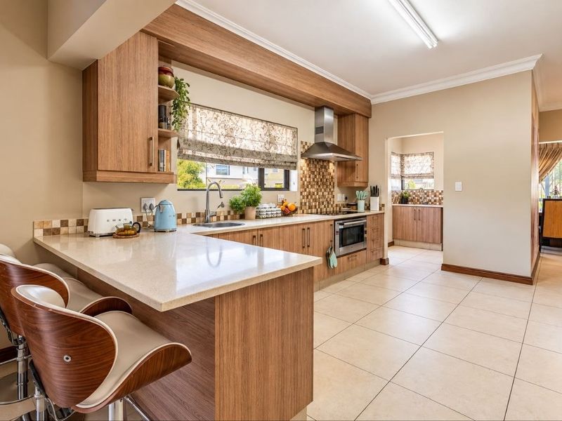Modern kitchen featuring wood-finish cabinetry, stone countertops, a breakfast bar, and integrated appliances, with an adjoining scullery area.