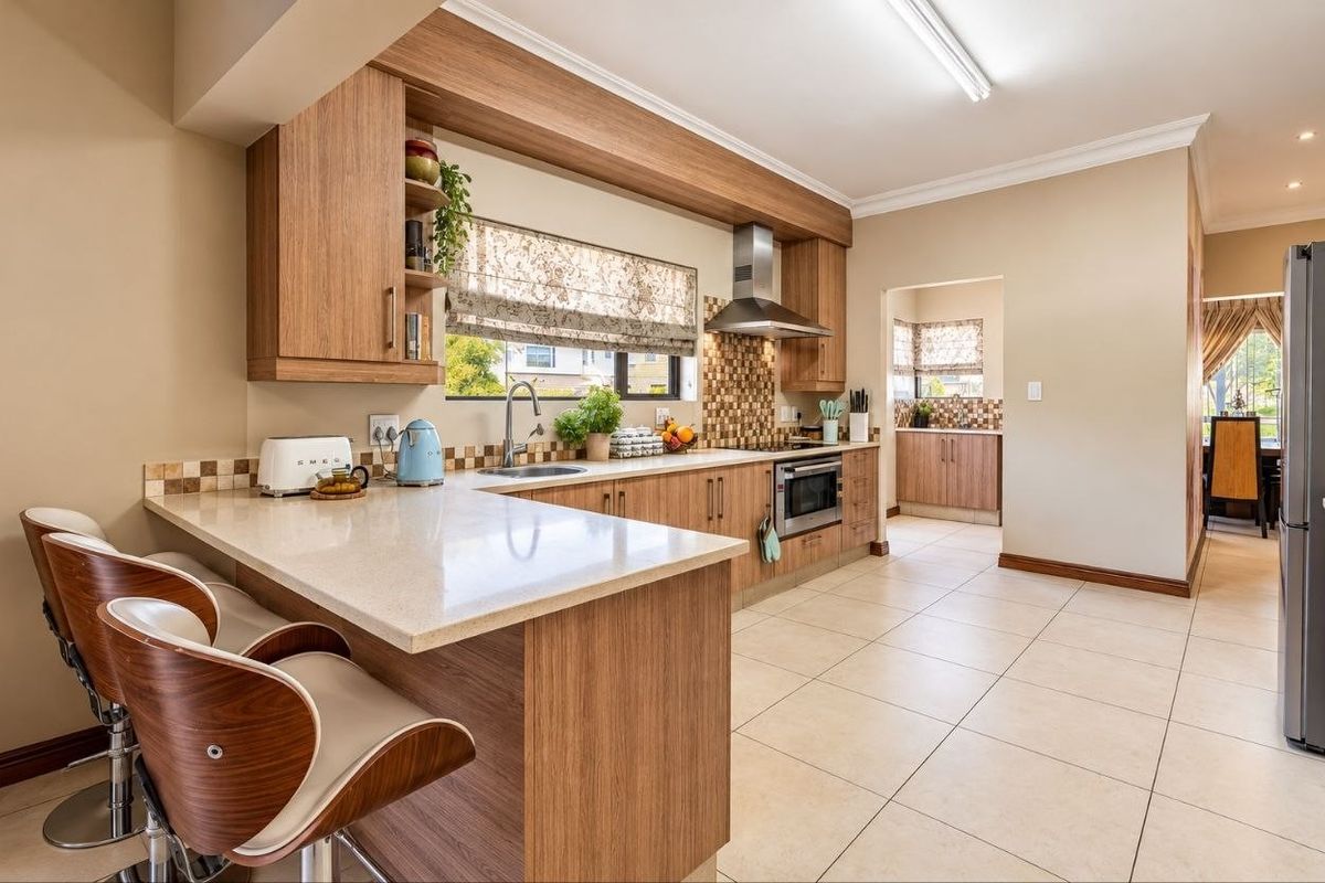 Modern kitchen featuring wood-finish cabinetry, stone countertops, a breakfast bar, and integrated appliances, with an adjoining scullery area.