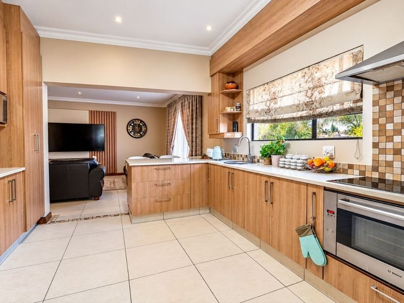 Modern open-plan kitchen featuring wood-finish cabinetry, stone countertops, integrated appliances, and tiled flooring, seamlessly flowing into the adjacent living area.