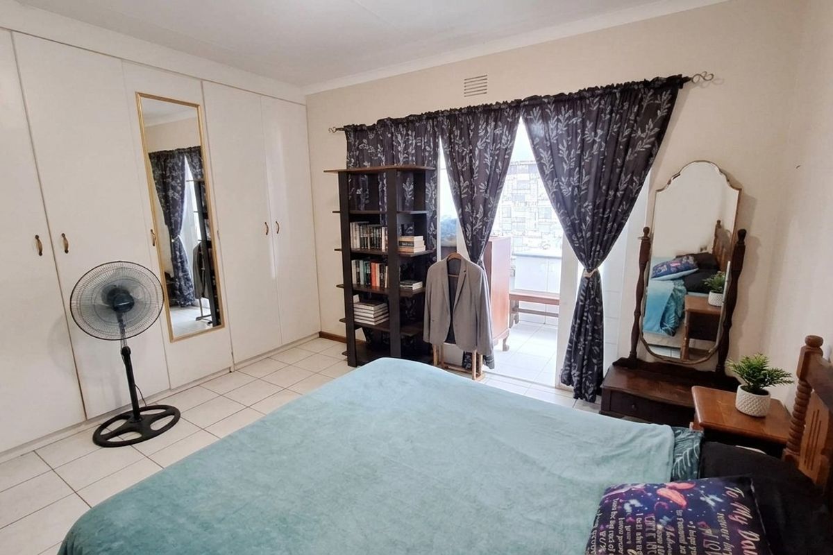 A bedroom featuring built-in cupboards, tiled flooring, and direct access to a balcony through a sliding door.