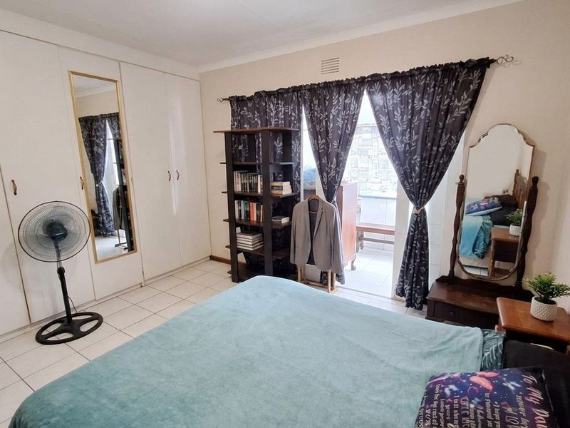 A bedroom featuring built-in cupboards, tiled flooring, and direct access to a balcony through a sliding door.