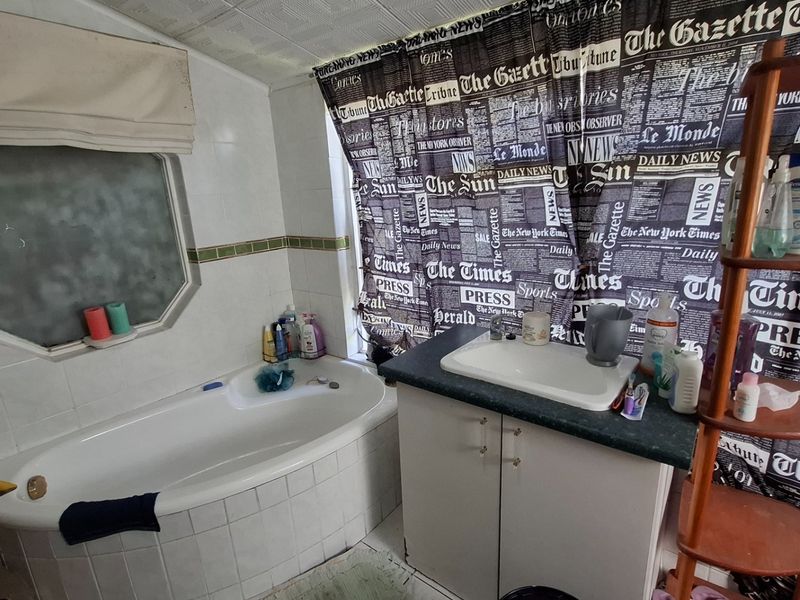 A dated bathroom featuring a built-in bathtub with tiled surround and a vanity cabinet with a drop-in sink.