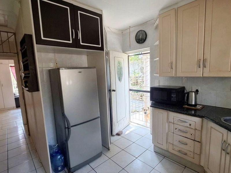 A functional kitchen featuring built-in cabinetry, granite countertops, and tiled flooring, with direct access to the exterior through a security gate.