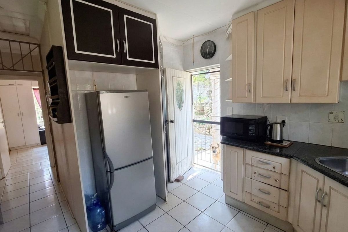 A functional kitchen featuring built-in cabinetry, granite countertops, and tiled flooring, with direct access to the exterior through a security gate.