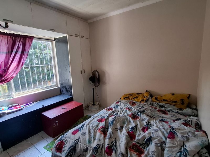 A bedroom featuring built-in cupboards, tiled flooring, and a window with security bars, requiring cosmetic updates to improve its overall condition.