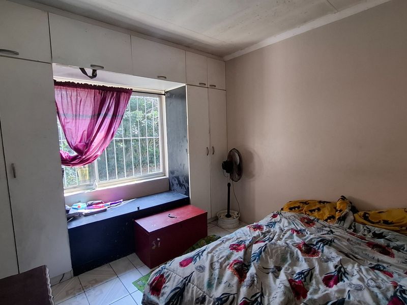 Bedroom featuring built-in cupboards, tiled flooring, and a window with security bars. The room requires cosmetic updates to improve its overall condition.