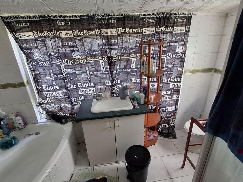 A dated bathroom featuring a built-in vanity with sink, a bathtub, and tiled wall finishes, requiring cosmetic updates to modernize the space.