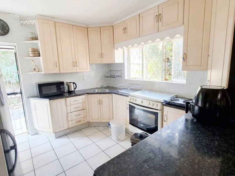 Functional kitchen featuring light-toned cabinetry, dark granite-look countertops, tiled flooring, and a freestanding oven, with direct access to the exterior.