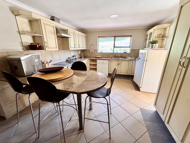 A functional kitchen featuring built-in cabinetry, tiled backsplash, integrated hob and oven, and a central dining area with tiled flooring.