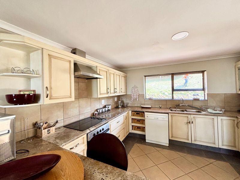 A functional kitchen featuring light-toned cabinetry, granite countertops, a tiled backsplash, and integrated cooking appliances with a double basin sink.