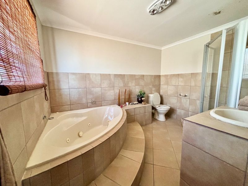 Spacious bathroom featuring a corner spa bath, separate shower enclosure, tiled vanity, and neutral wall tiling throughout.