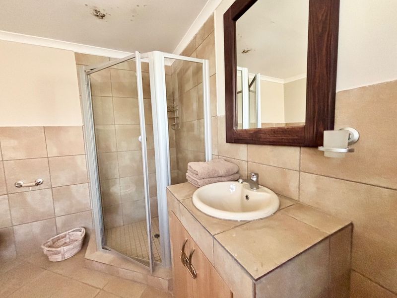 Bathroom featuring a tiled shower enclosure, vanity cabinet with drop-in basin, and wall-mounted mirror. Note visible ceiling water damage requiring attention.